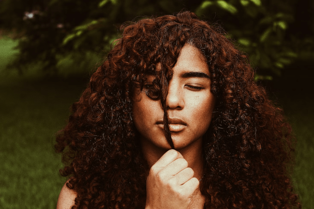 A woman pulling out a strand from her curly brown hair.