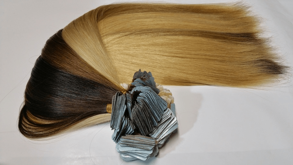 A bundle of brown, black, and blonde tape hair extensions.